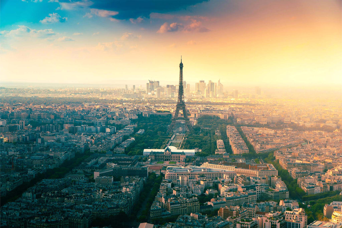 Aerial view of Paris with the Eiffel Tower centered, surrounded by dense city buildings and roads under a dramatic sky with blue, orange, and golden light.