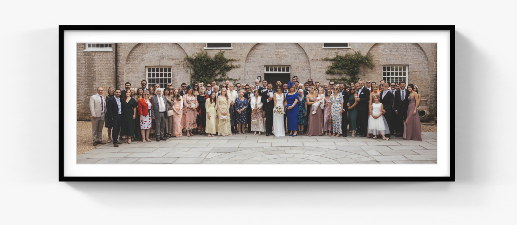 Panoramic wedding group photograph displayed in a black frame with a white mount.