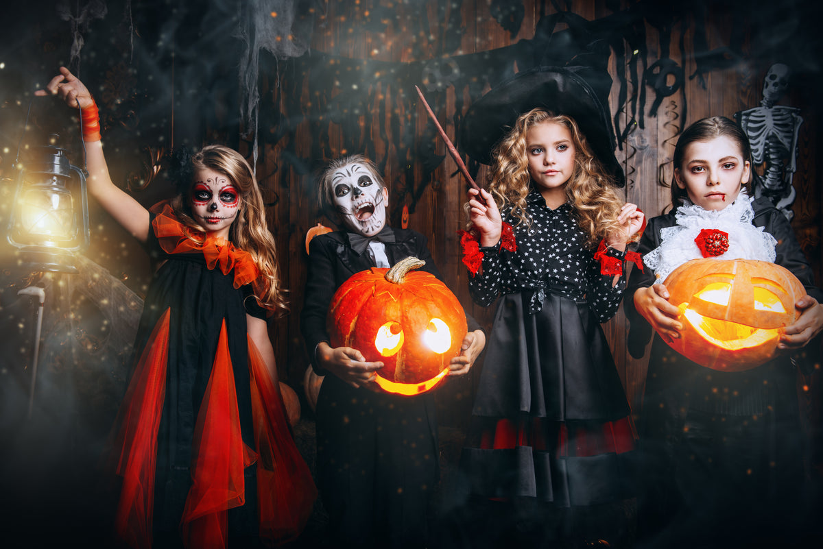 Four children in Halloween costumes holding pumpkins and a lantern